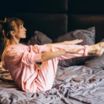 女子在床上進行睡前伸展動作，抬起雙腿與雙臂保持平衡，進行放鬆運動