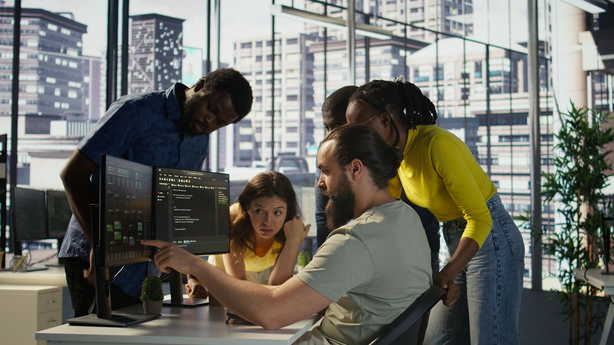 Software developers discussing code on multiple monitors in modern office